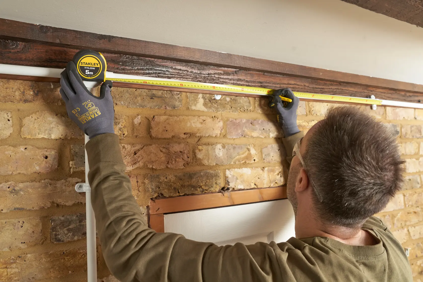 Photo of STANLEY 0-30-697 tape measure used to measure length above a brick wall indoors.