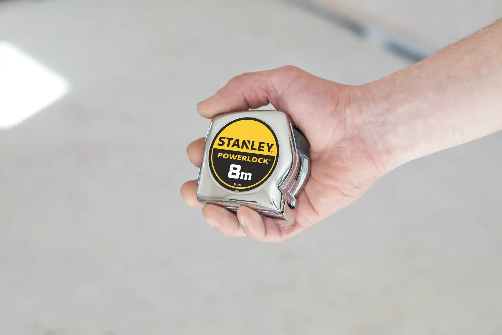 Stanley 0-33-198 Powerlock 8m tape measure held in hand, chrome finish, product photography.