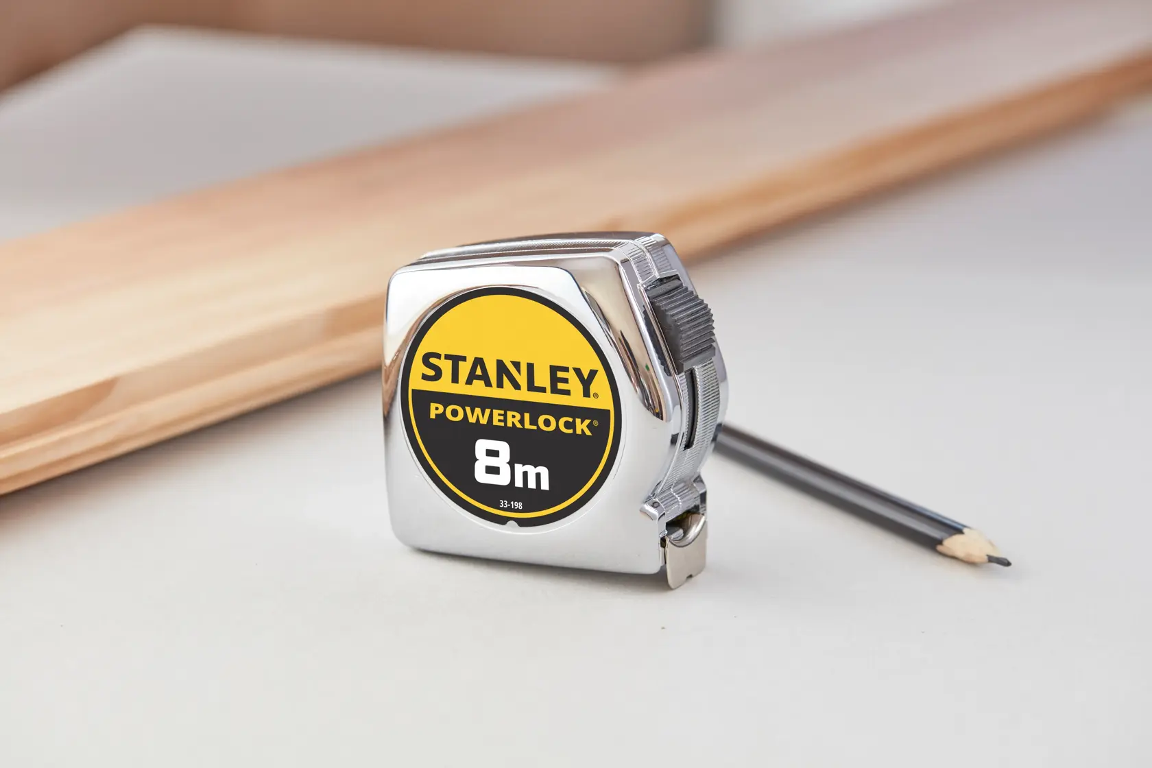 STANLEY 0-33-198 PowerLock 8m tape measure with chrome case, shown on tabletop with pencil and wood piece.