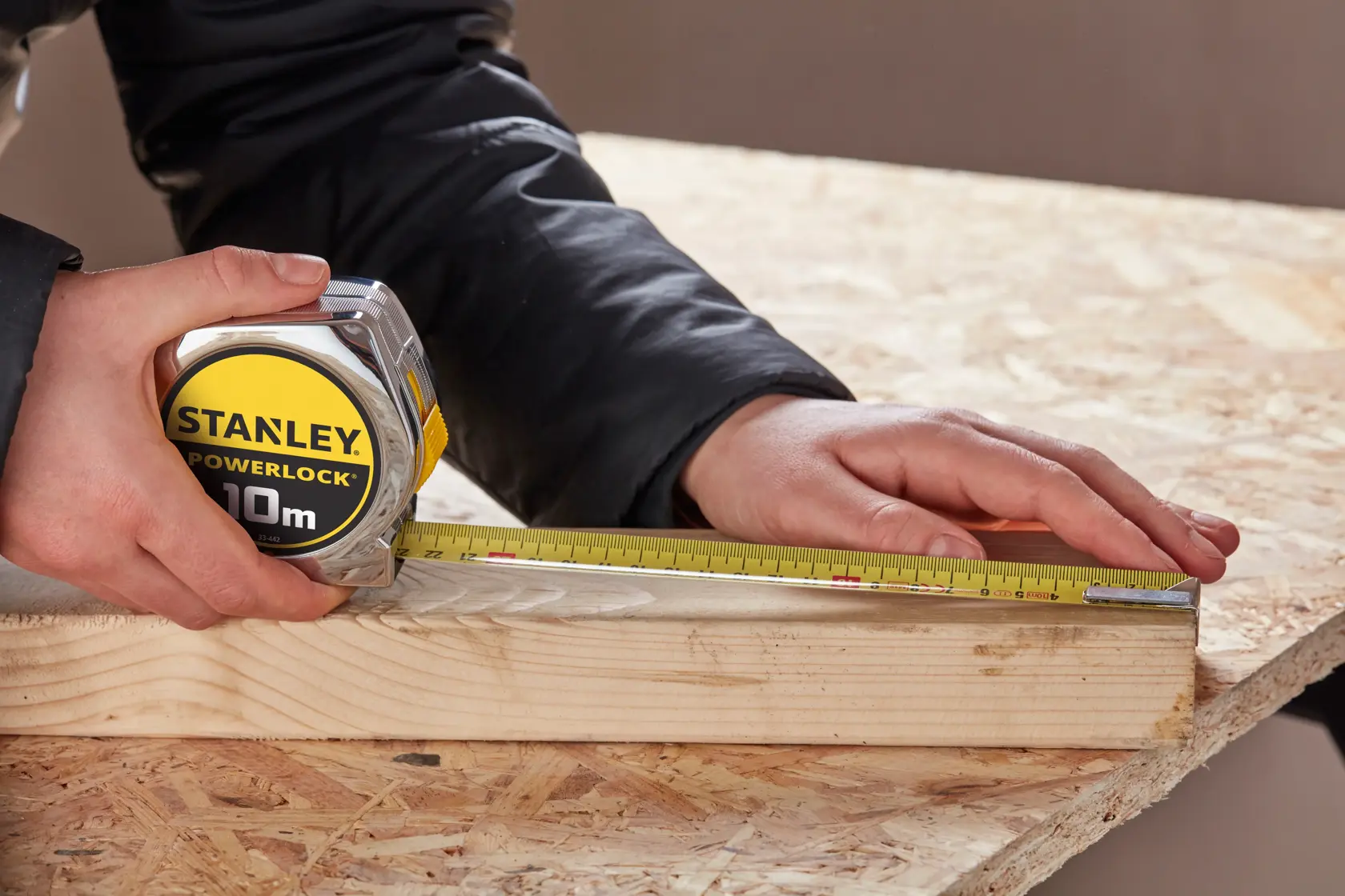 Photo of STANLEY 0-33-442 tape measure being used to measure a wooden plank on a workbench.