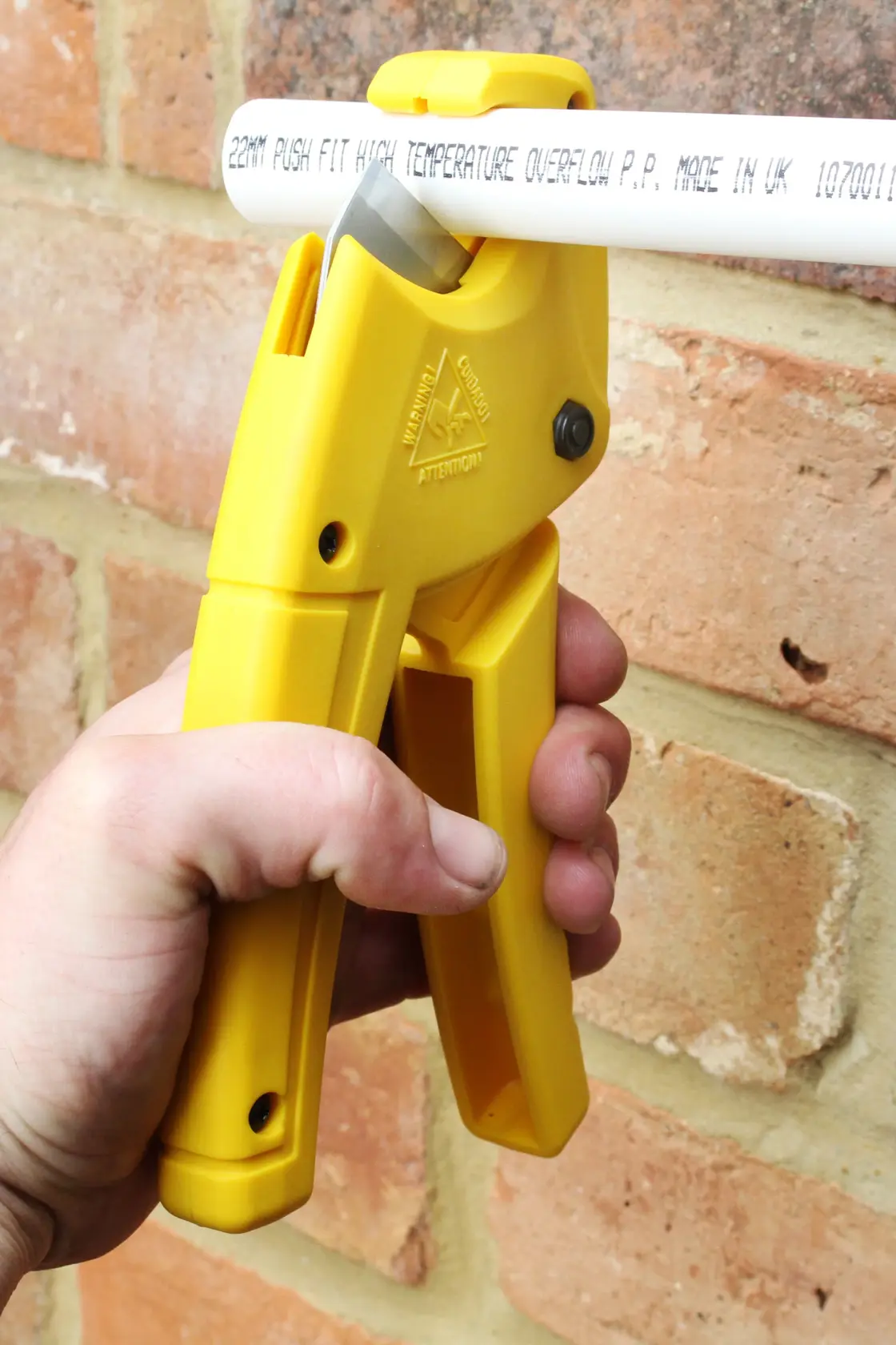 STANLEY 0-70-450 yellow plastic pipe cutter held in hand, cutting white pipe, close-up view.