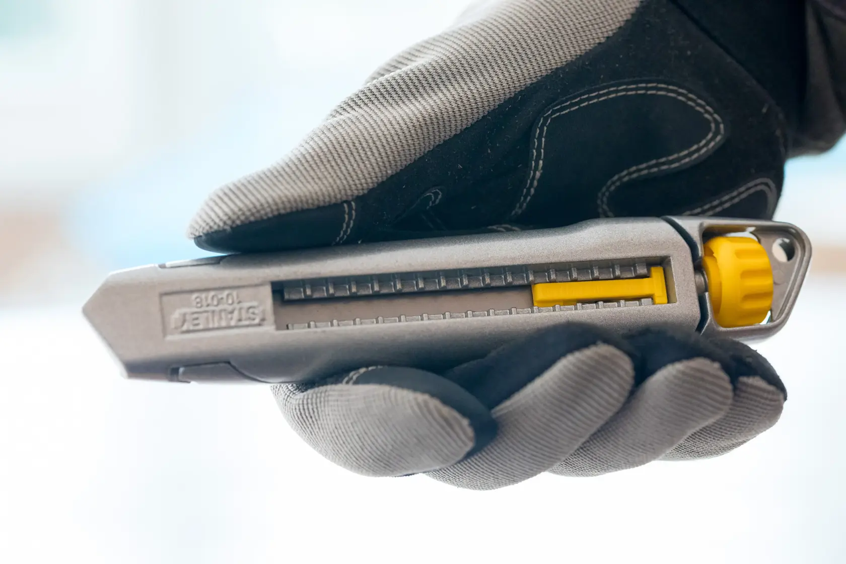 STANLEY 1-10-018 utility knife with gray and yellow details held in gloved hand, side angle.