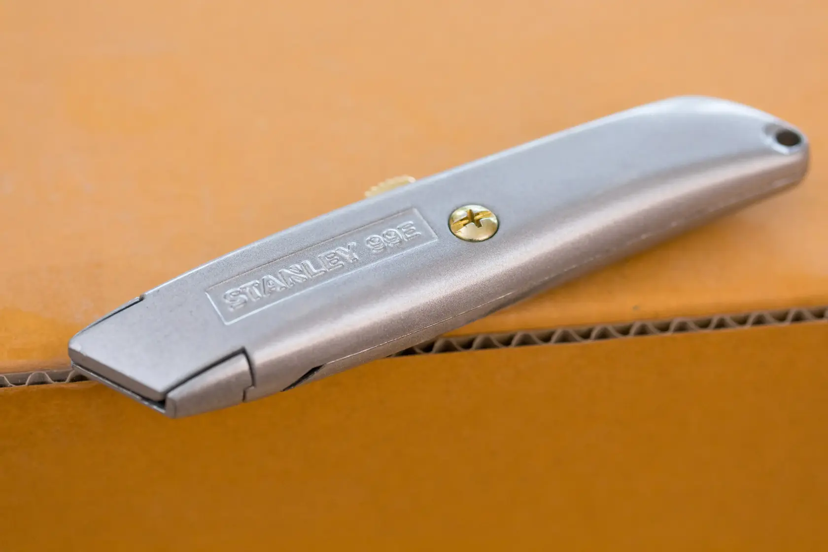 Photo of STANLEY 1-10-099 silver utility knife resting on a cardboard box, angled side view.
