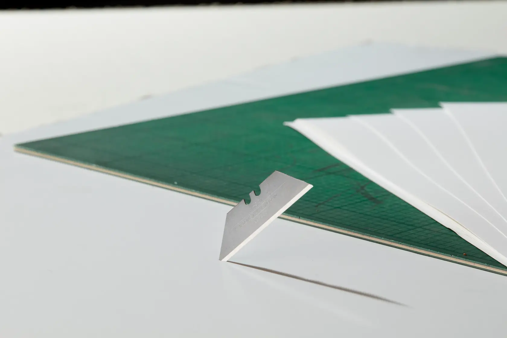 STANLEY 1-11-916 utility blade with paper sheets and green cutting mat, side view photography.
