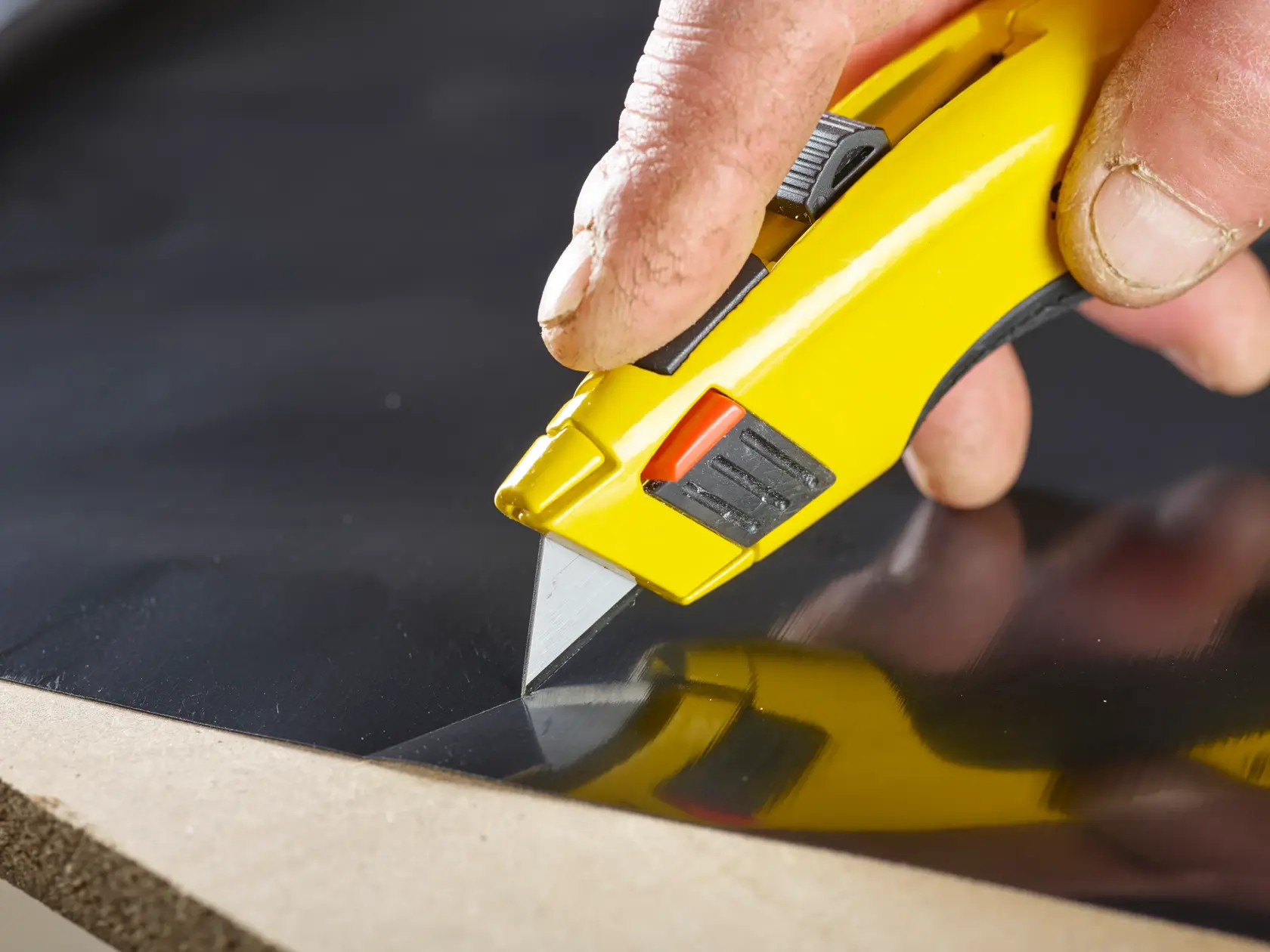 STANLEY 1-11-916 utility knife in yellow cutting black material, close-up showing hand grip.