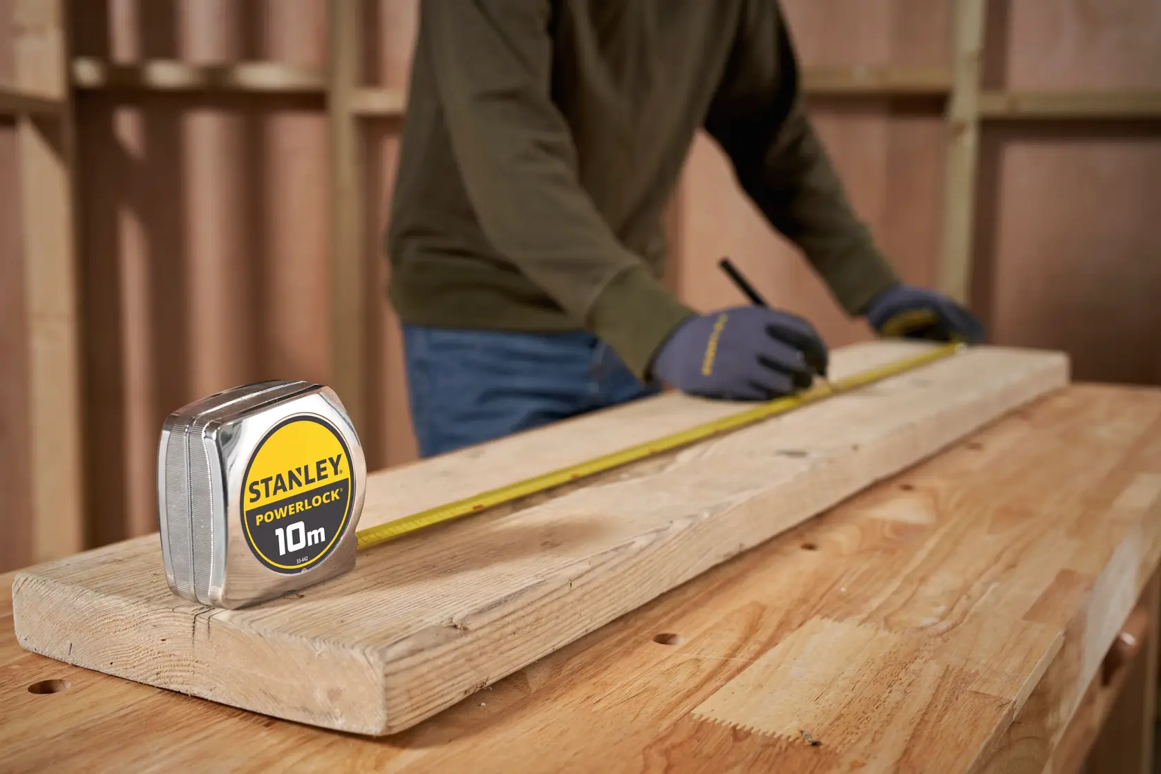 Photo of STANLEY 1-33-442 tape measure on wood, worker marking plank in workshop.