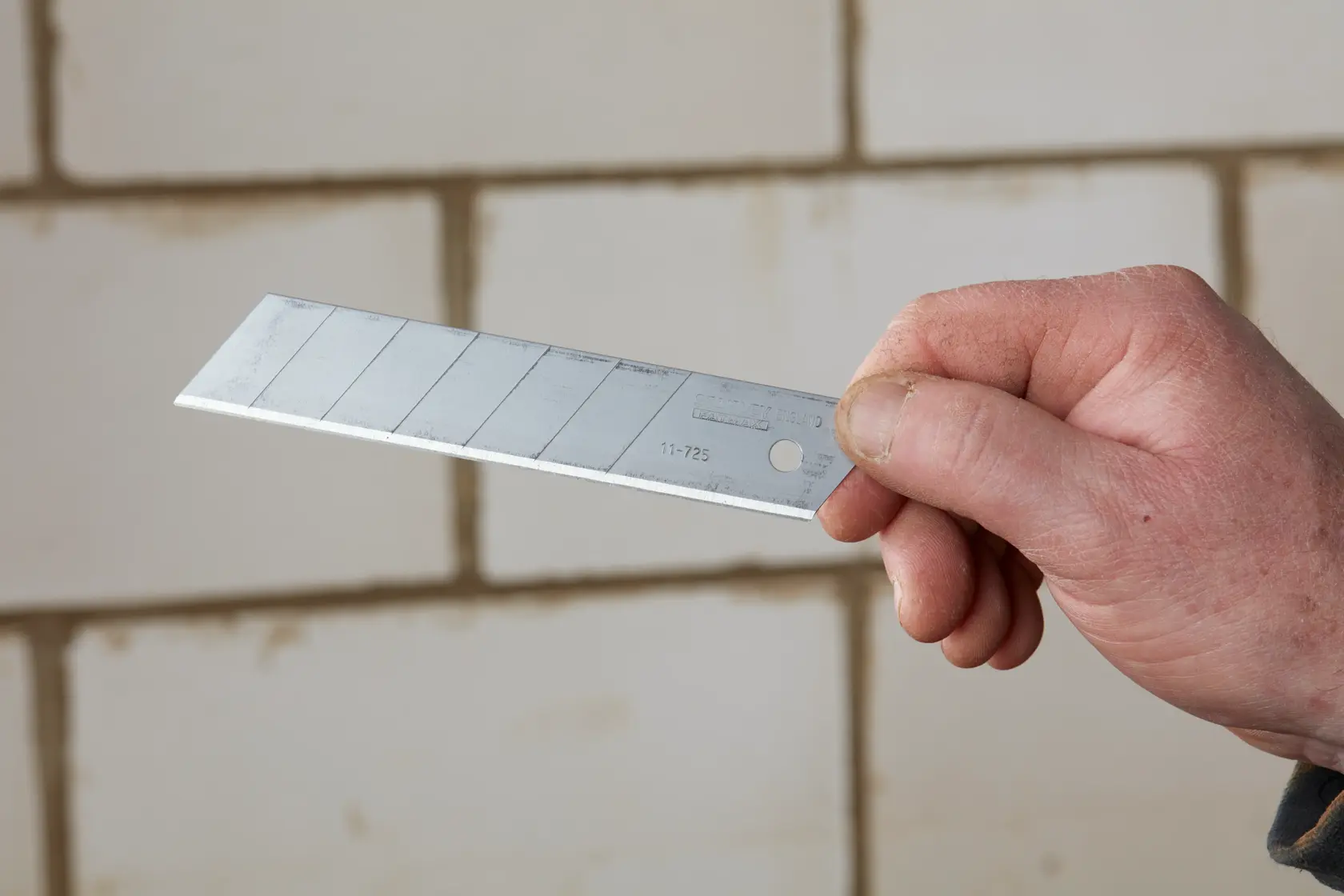 Photo of STANLEY 2-11-725 snap-off utility knife blade held in a hand, shown against a brick wall.
