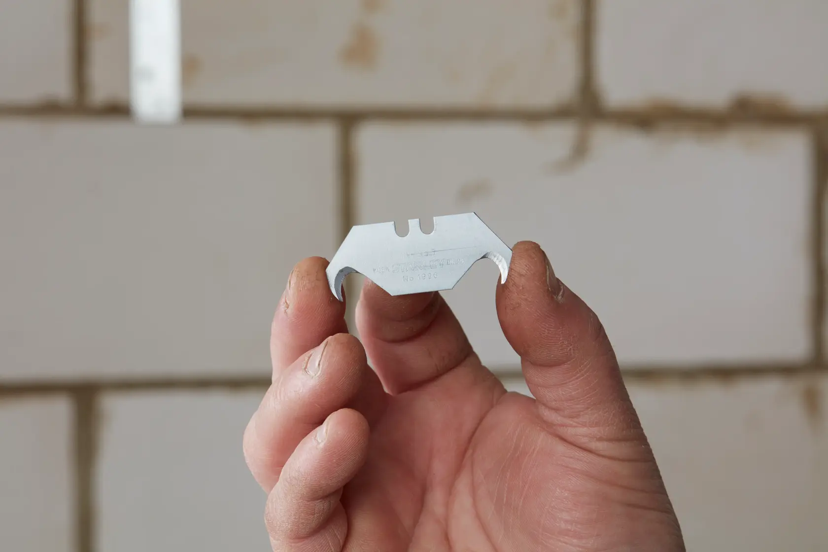 Photo of STANLEY 2-11-983 hook blade held in hand, used for cutting, shown against tiled background.