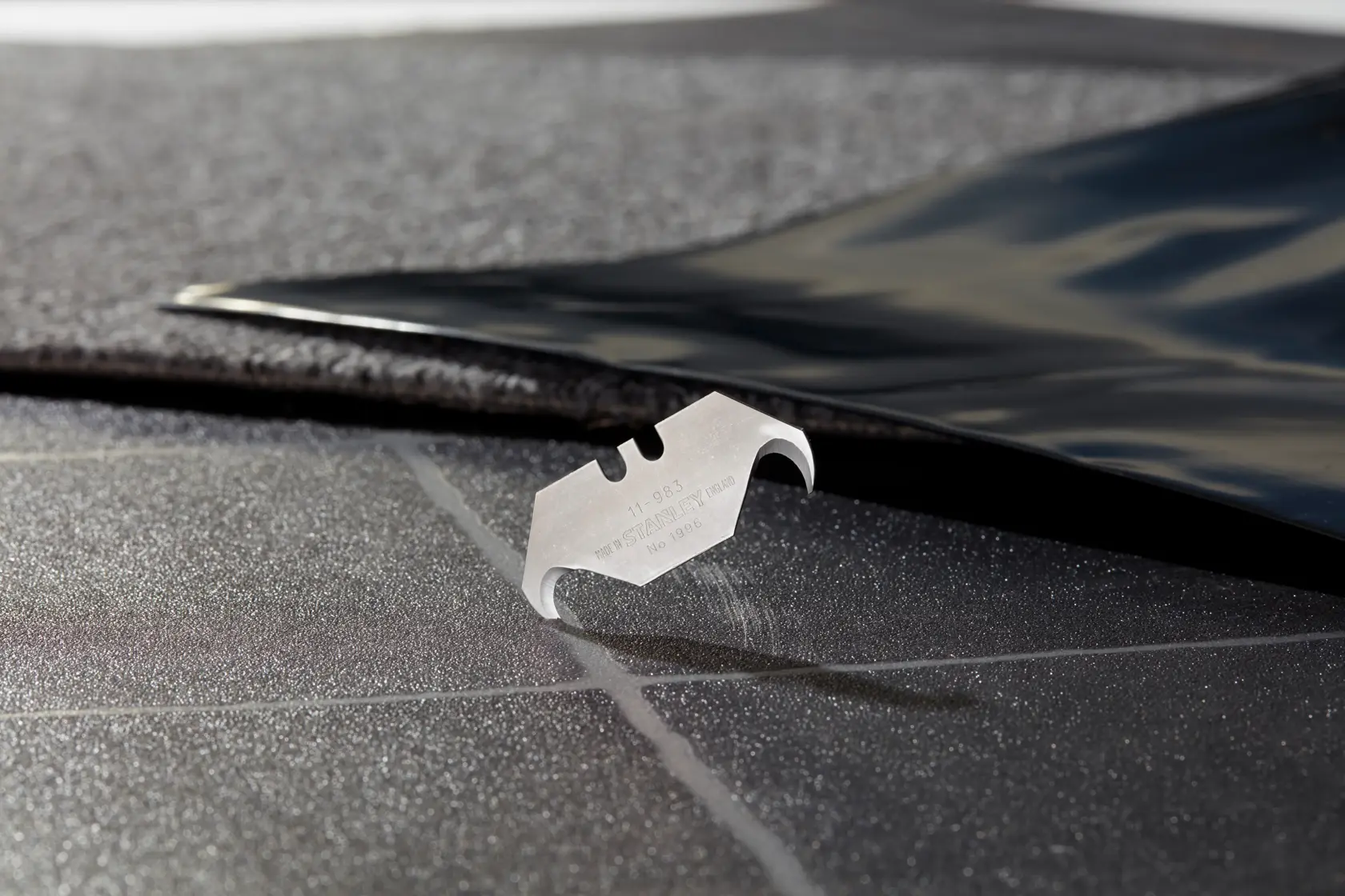 STANLEY 2-11-983 utility blade on a textured black surface, close-up angle, product photography.