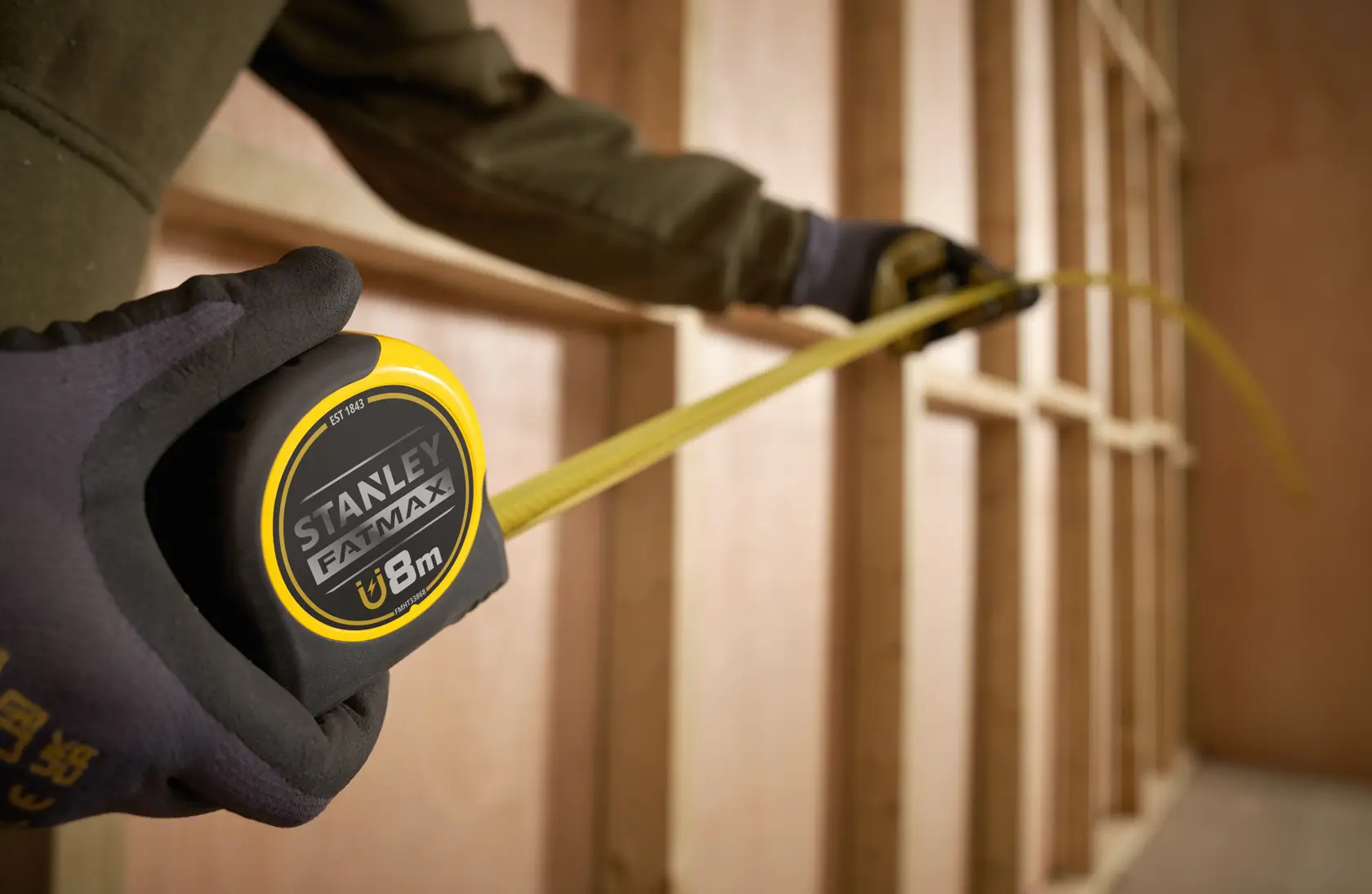 Stanley FMHT0-33868 tape measure with yellow blade extended in a construction framing setting.