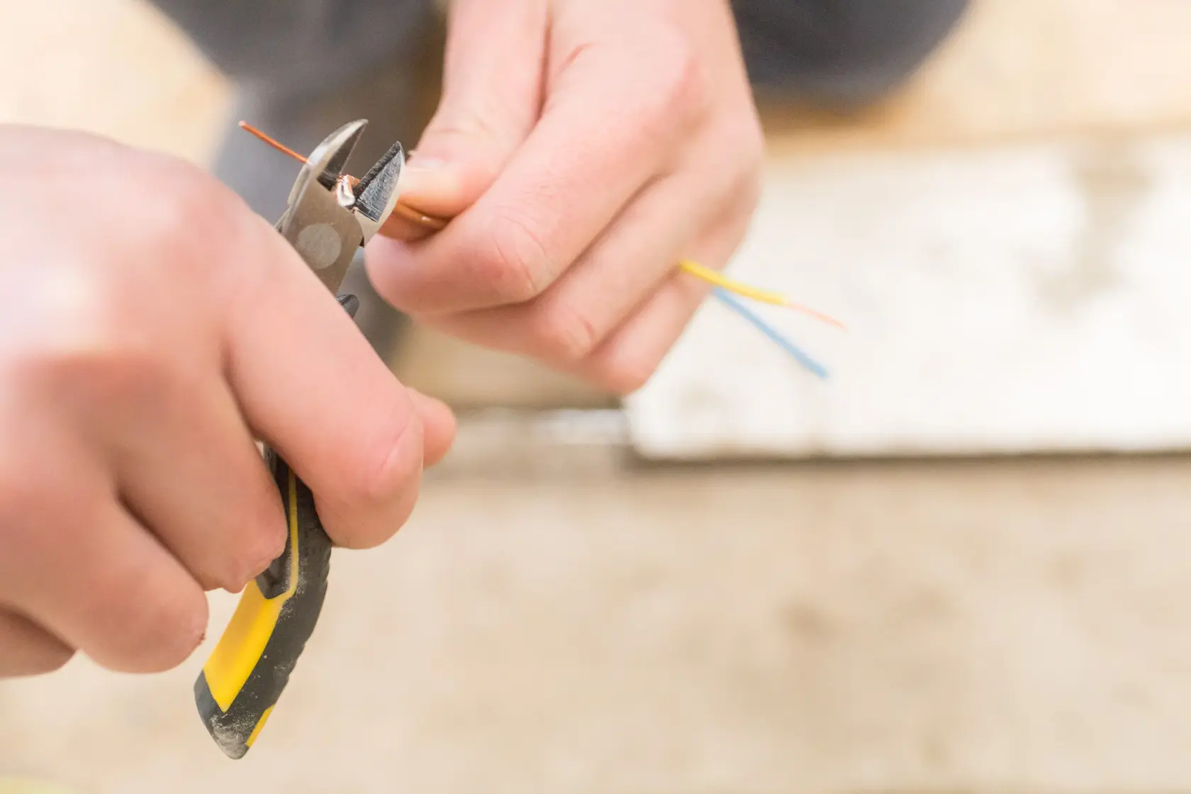 STANLEY FMHT0-80518 diagonal pliers held cutting colored electrical wires, close-up photo.