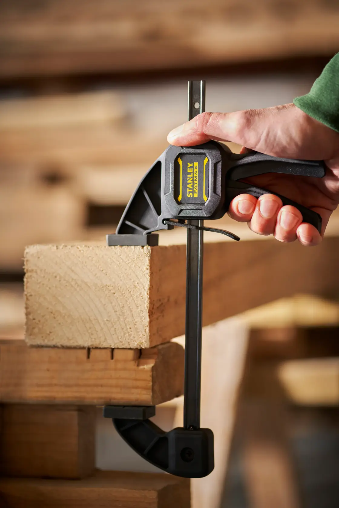 STANLEY FMHT0-83232 photography of quick grip clamp securing a wooden plank in workshop setting.