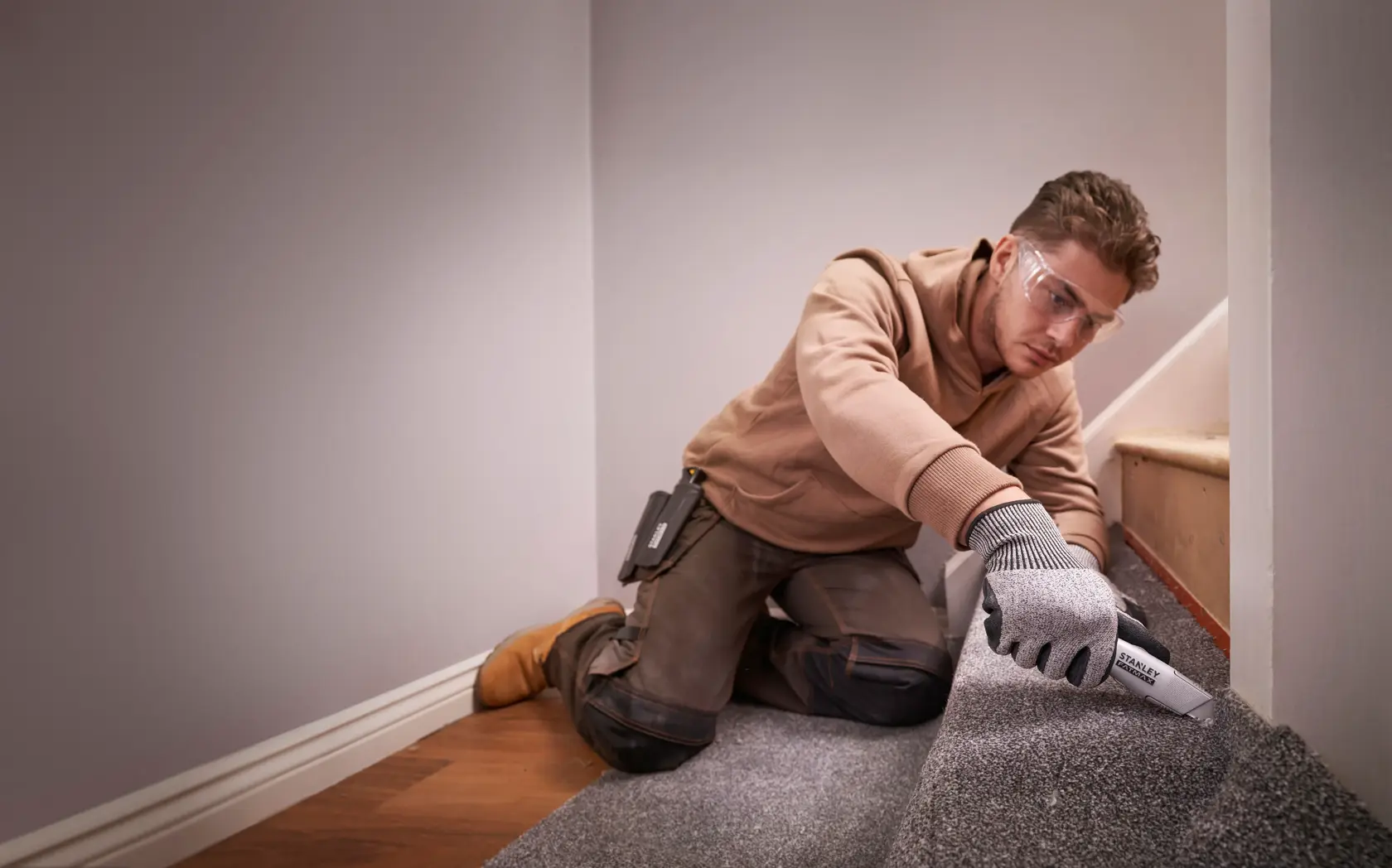 Photo of a worker using a STANLEY FMHT10501-0 utility knife to cut carpet on stairs.