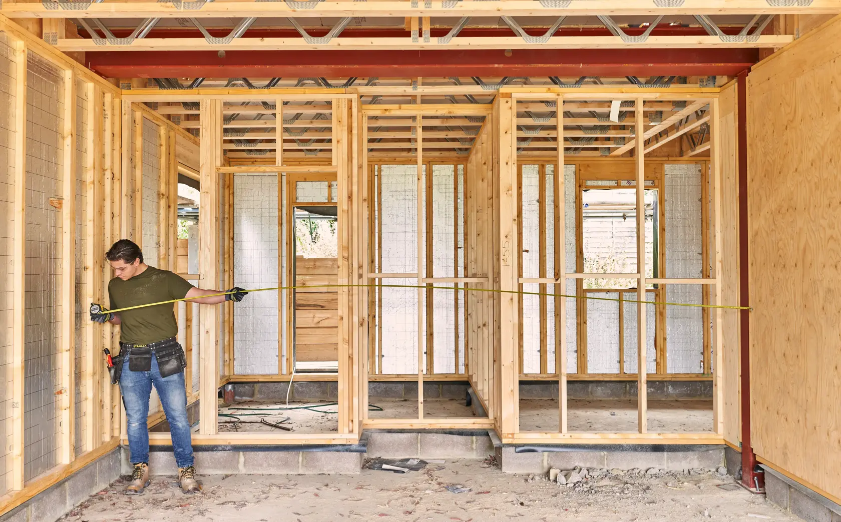 STANLEY FMHT38217-0 tape measure used by worker in wooden house construction site, measuring wall frame.