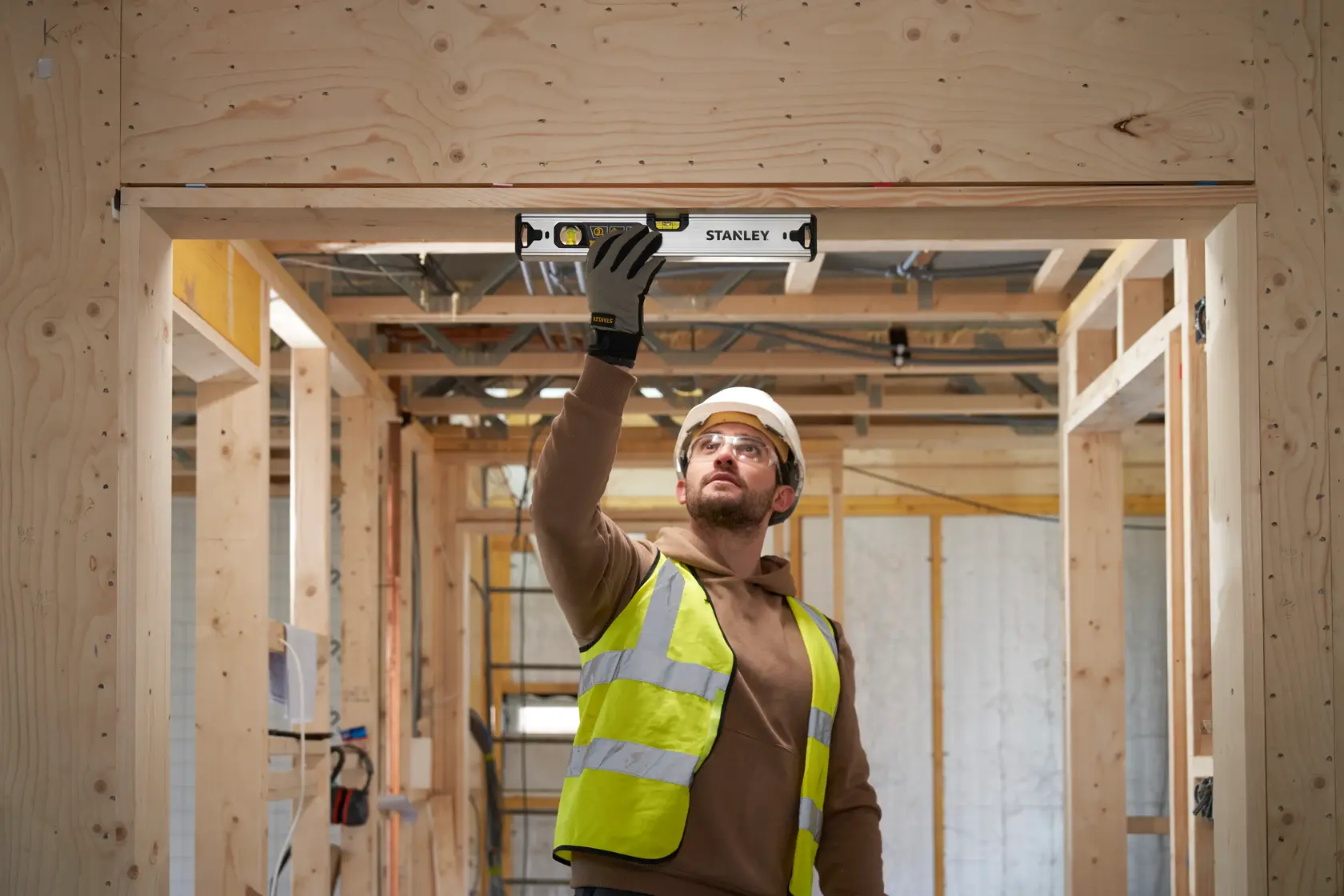 Photo of a worker using a STANLEY FMHT43671-1 spirit level on a wooden door frame at a construction site.