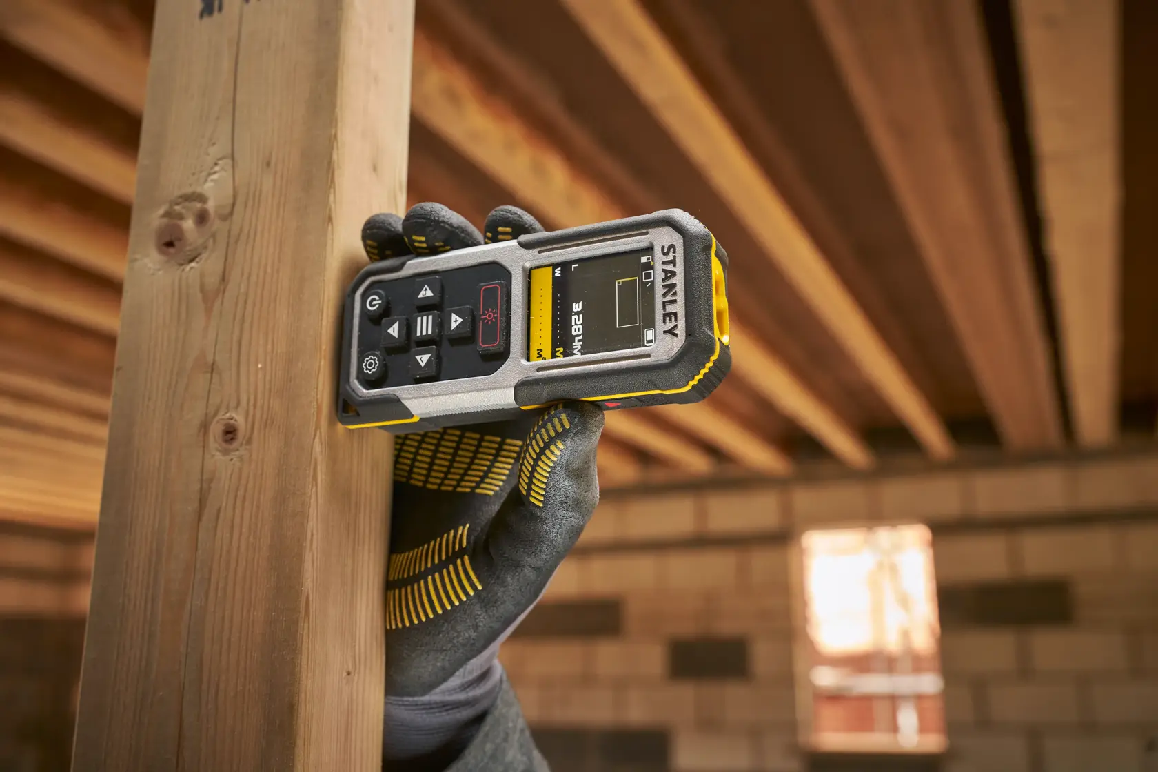 Photo of STANLEY FMHT77050-XJ laser distance measurer in use, showing display and buttons, held in a gloved hand.
