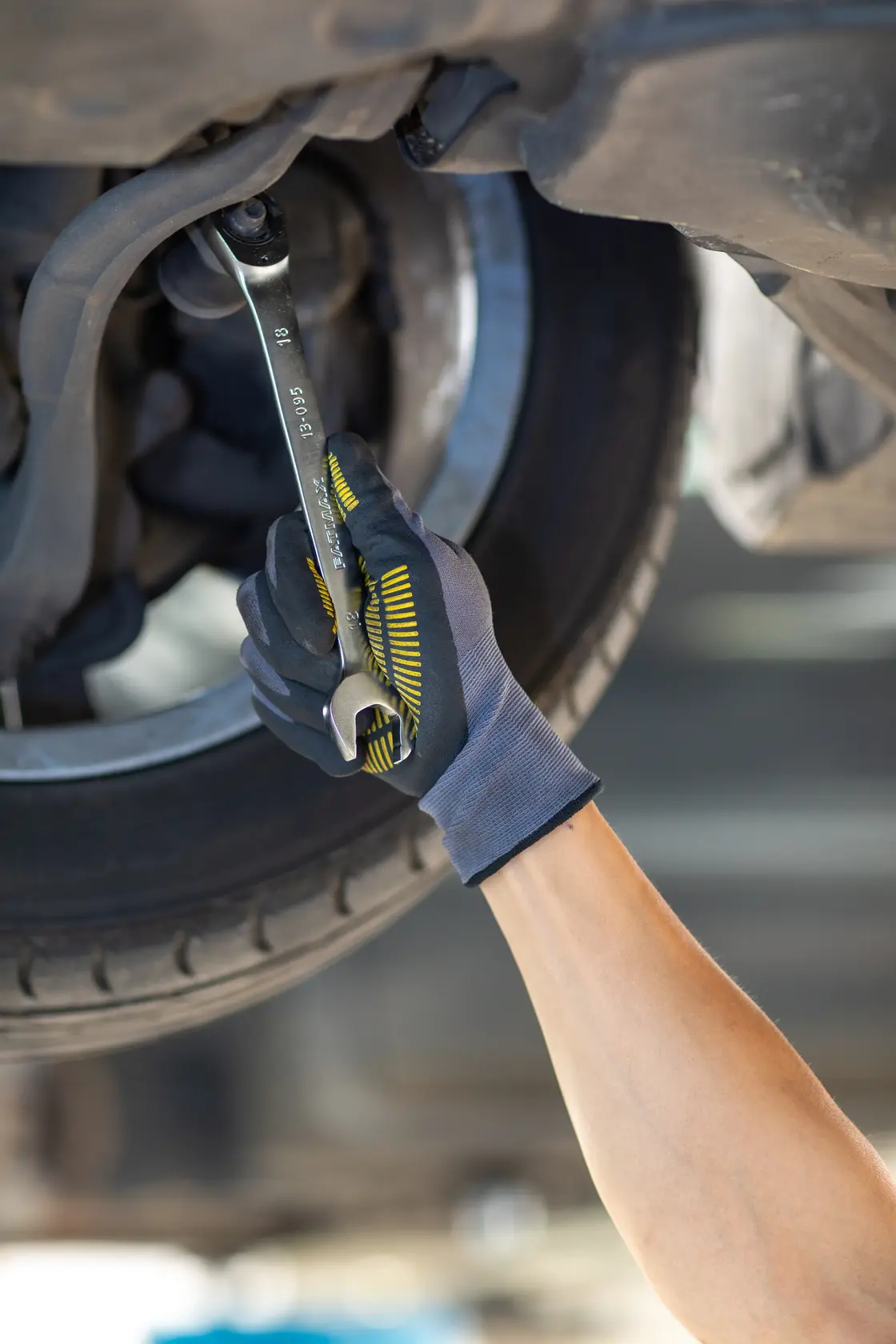 Photo of STANLEY FMMT13084-0 wrench used by a gloved hand tightening a nut under a car near the tire.