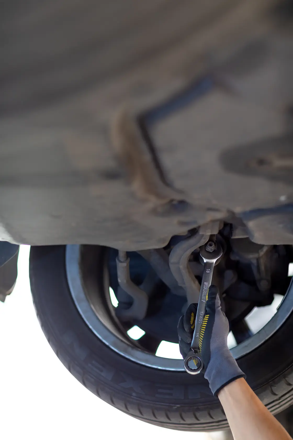 Photo of STANLEY FMMT13084-0 wrench used on car suspension by gloved hand, automotive context.