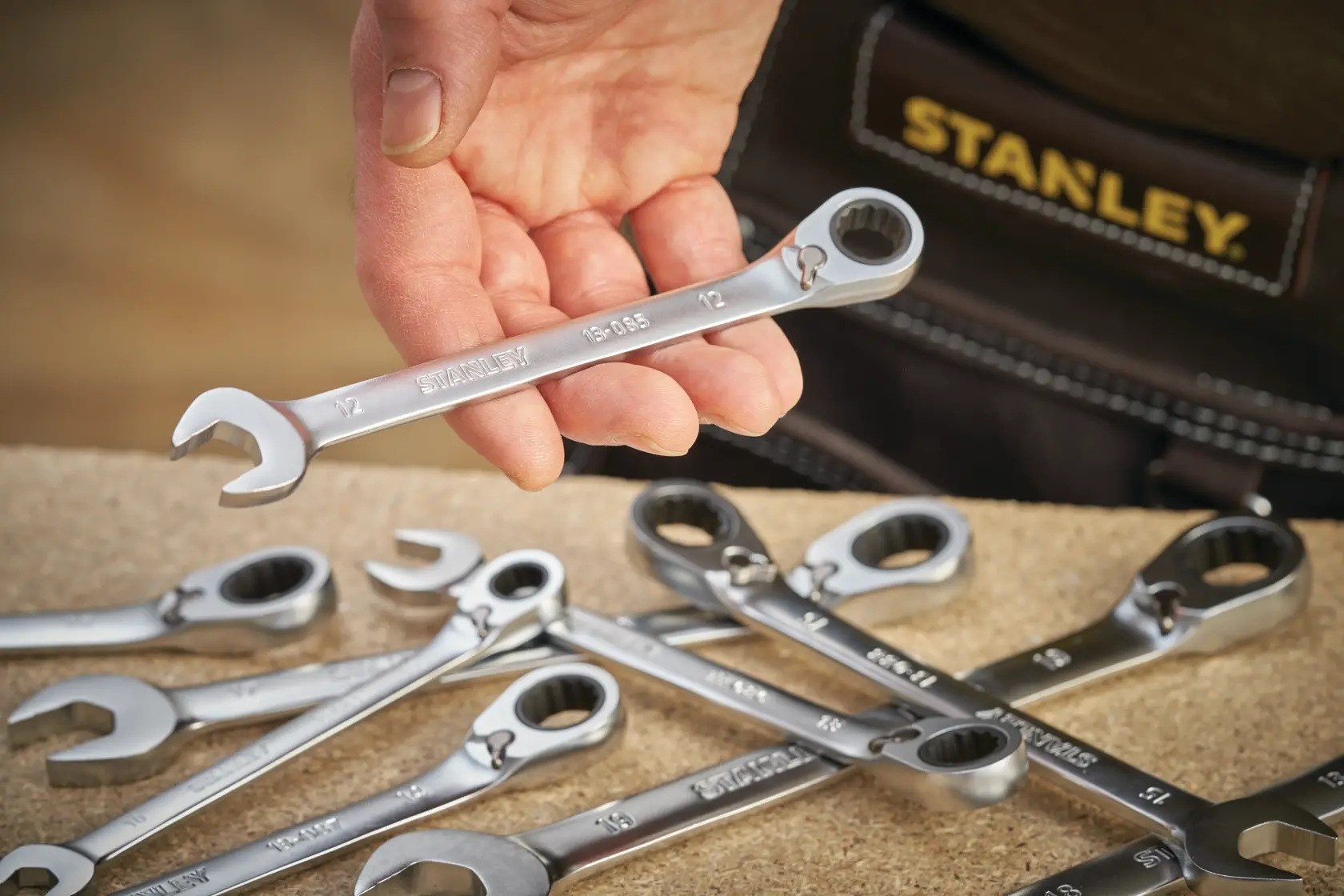 STANLEY FMMT13088-0 photography of a hand holding a combination wrench above several wrenches on a work surface.
