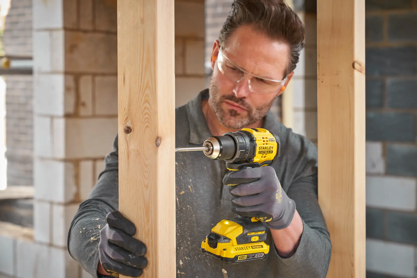 Photo of STANLEY SFMCD714B-XJ cordless drill in use drilling into wood at a construction site.