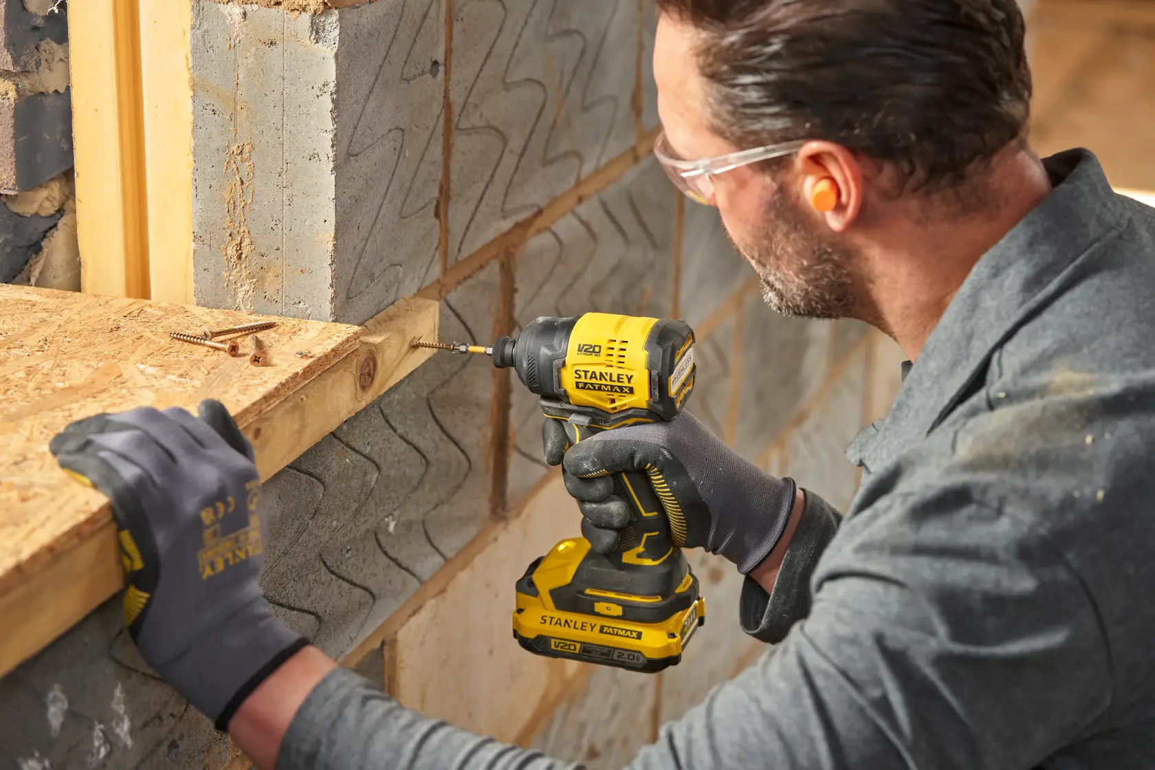 Photo of STANLEY SFMCF811D1T cordless impact driver in use, drilling into wood at a construction site.