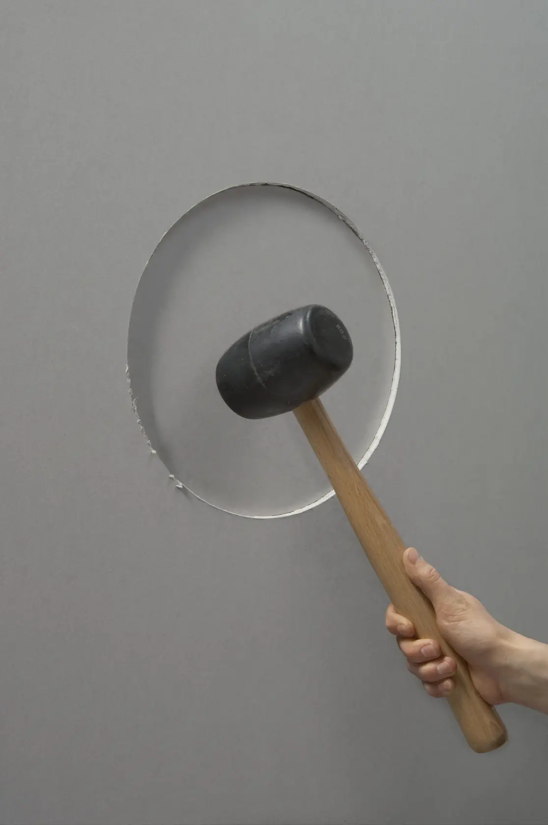 STANLEY STHT1-05878 rubber mallet with wooden handle, side view, held against a gray wall with a circular cutout.
