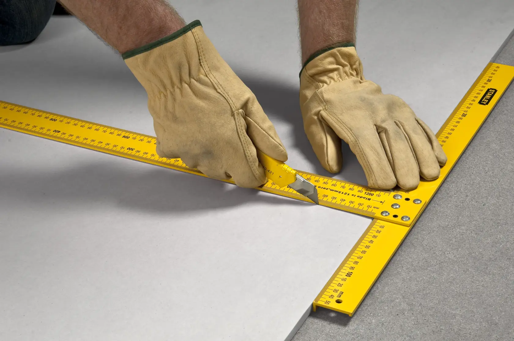STANLEY STHT1-05894 yellow drywall square used for cutting by gloved hands on a flat surface.