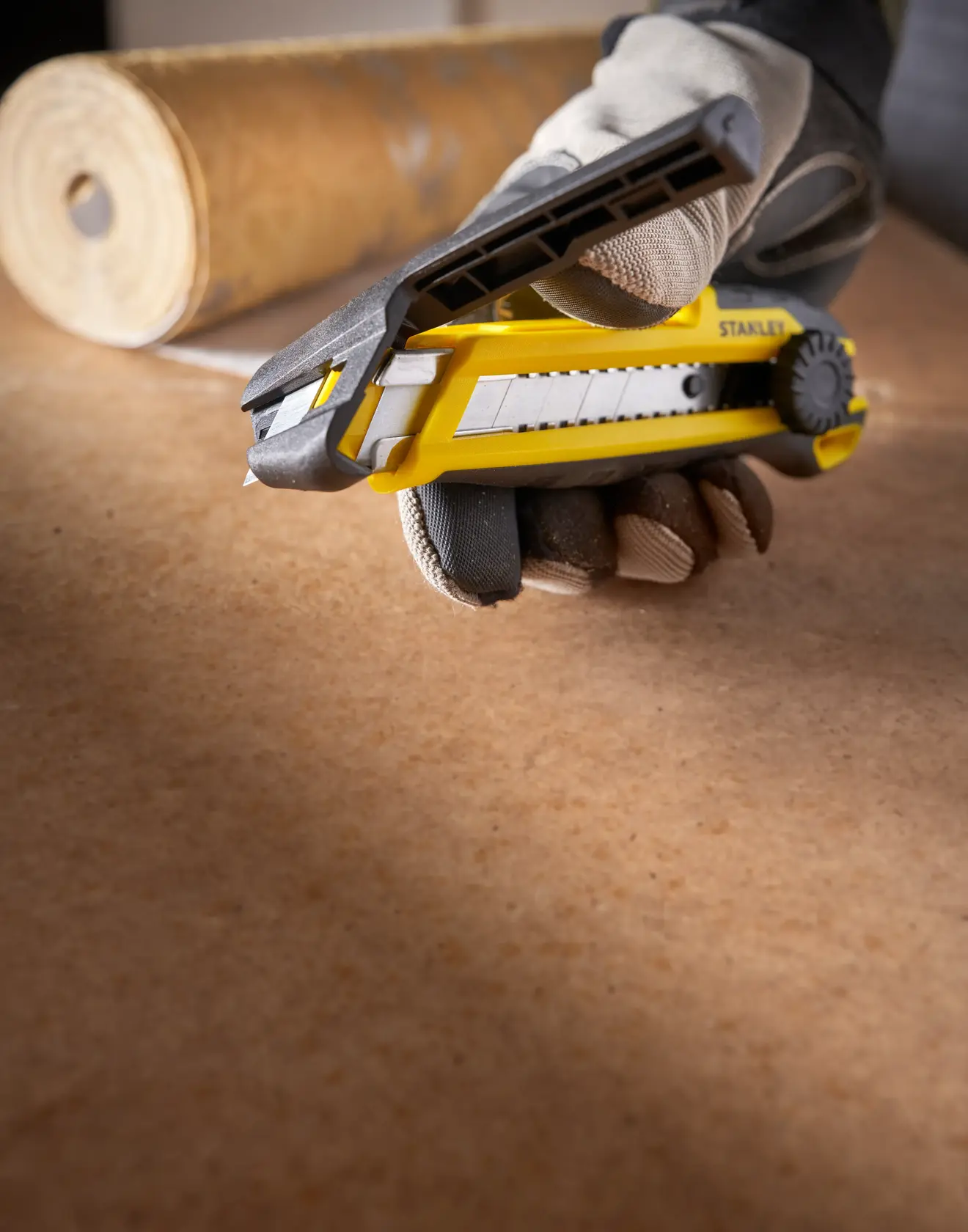 Photo of STANLEY STHT10500-0 utility knife in a gloved hand, yellow and black, on a work surface.