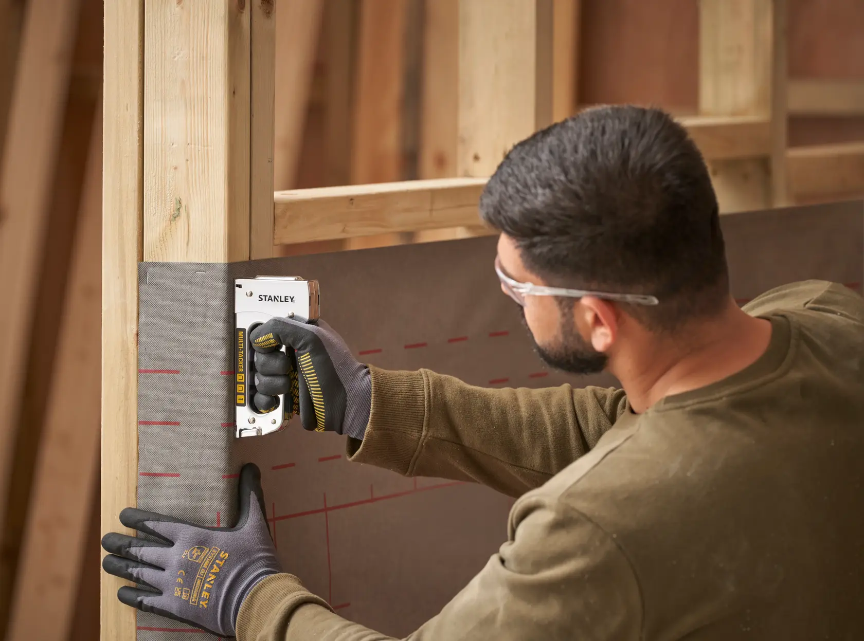 Stanley STHT6-70410 heavy-duty stapler used by person attaching material to wooden frame, construction context.