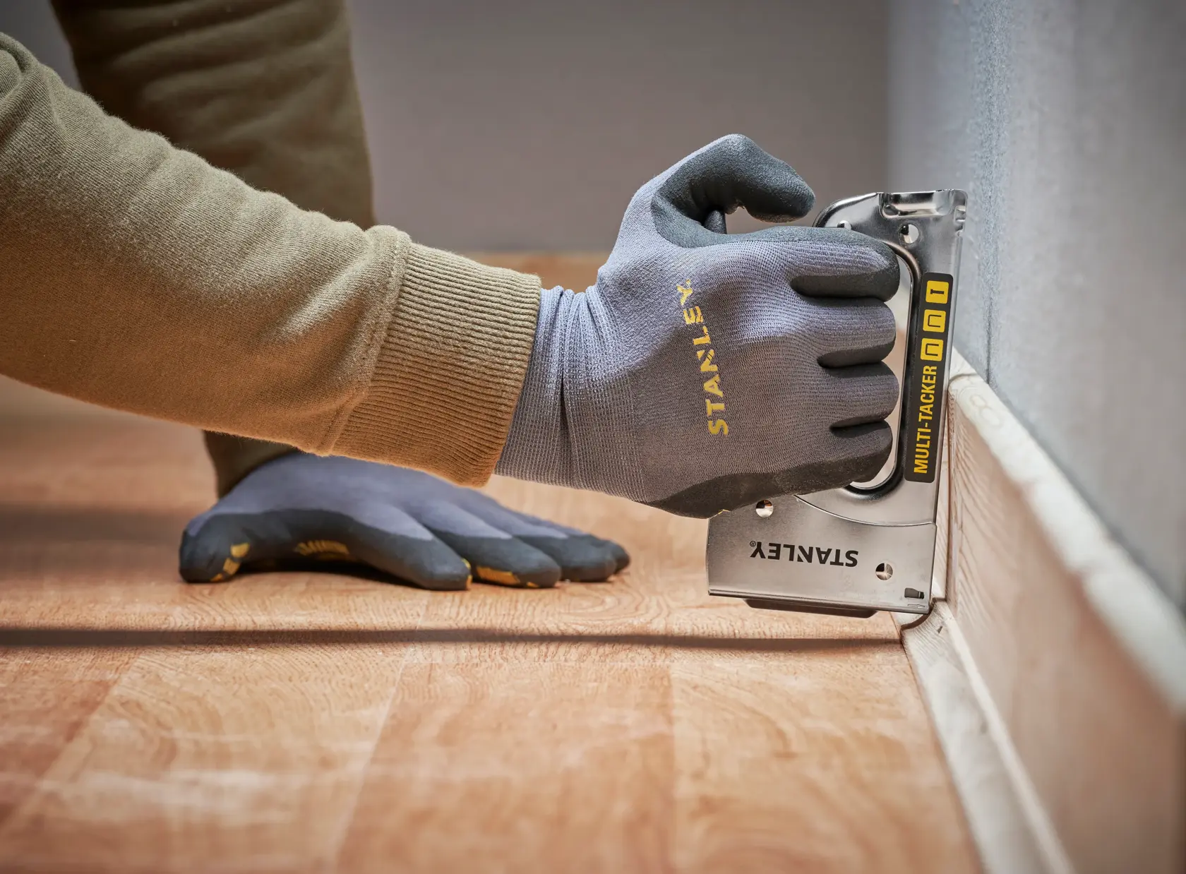 STANLEY STHT6-70410 multi-tacker used on floor trim, close-up angle, gloves visible.