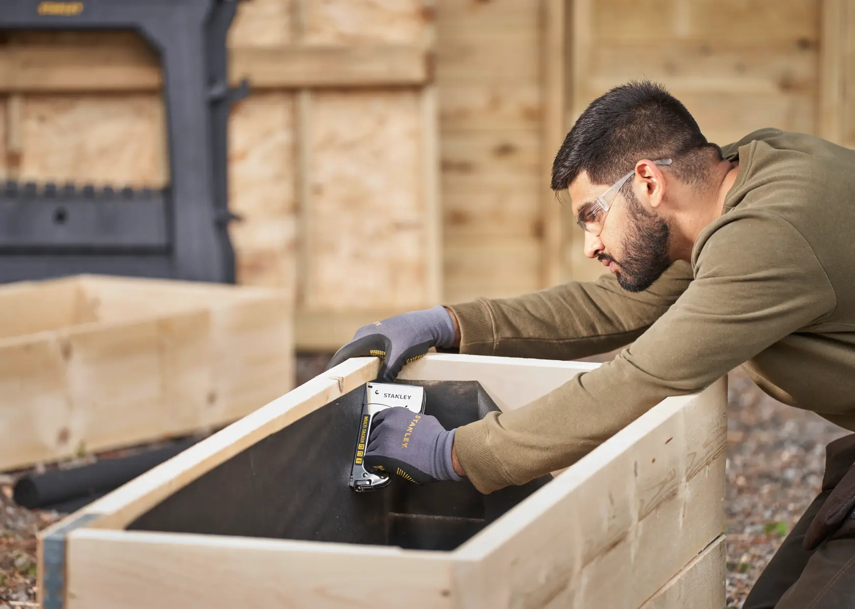 Photo of STANLEY STHT6-70410 hand stapler used for woodworking, person stapling liner inside wooden planter outdoors.