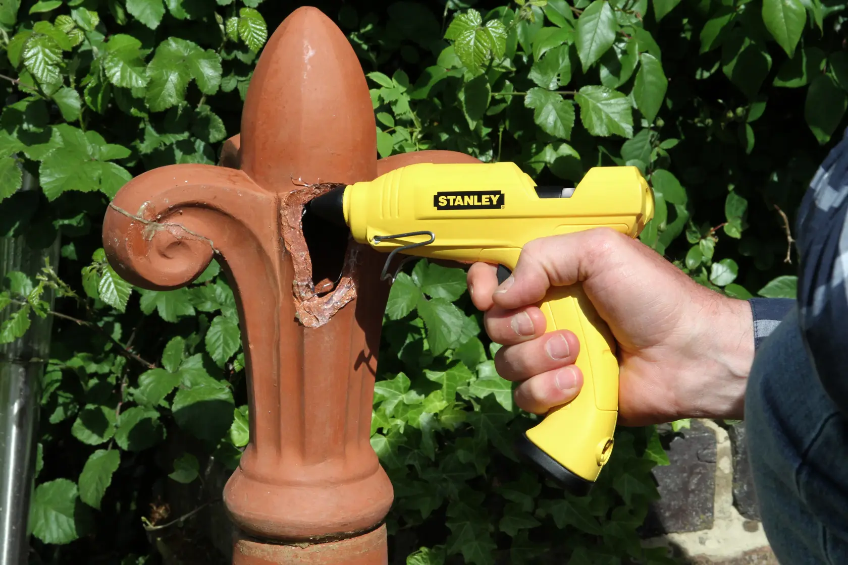Stanley STHT6-70416 yellow glue gun for repairing outdoor terracotta ornament, held by hand.