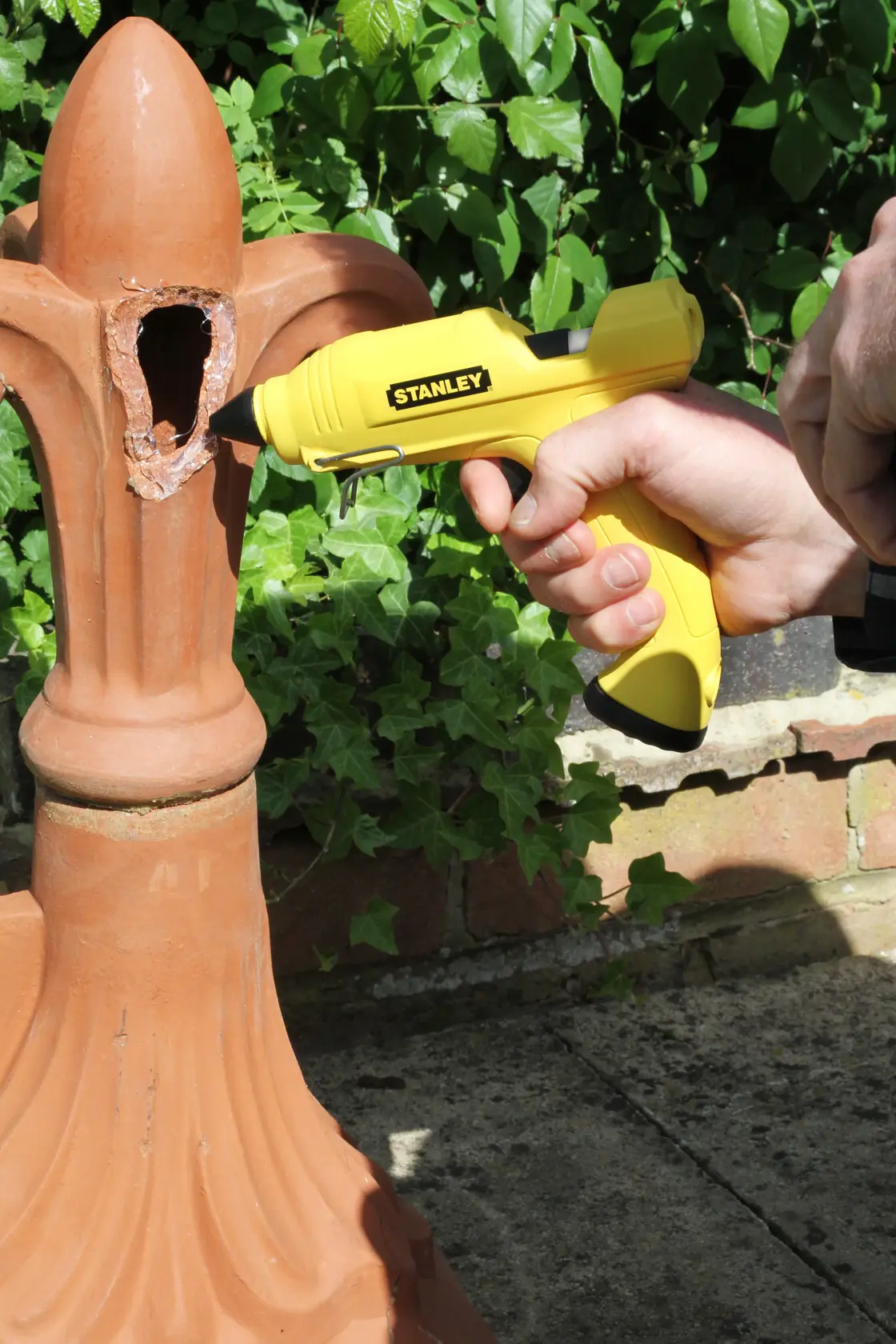 Stanley STHT6-70416 yellow glue gun used on damaged terracotta outdoors.