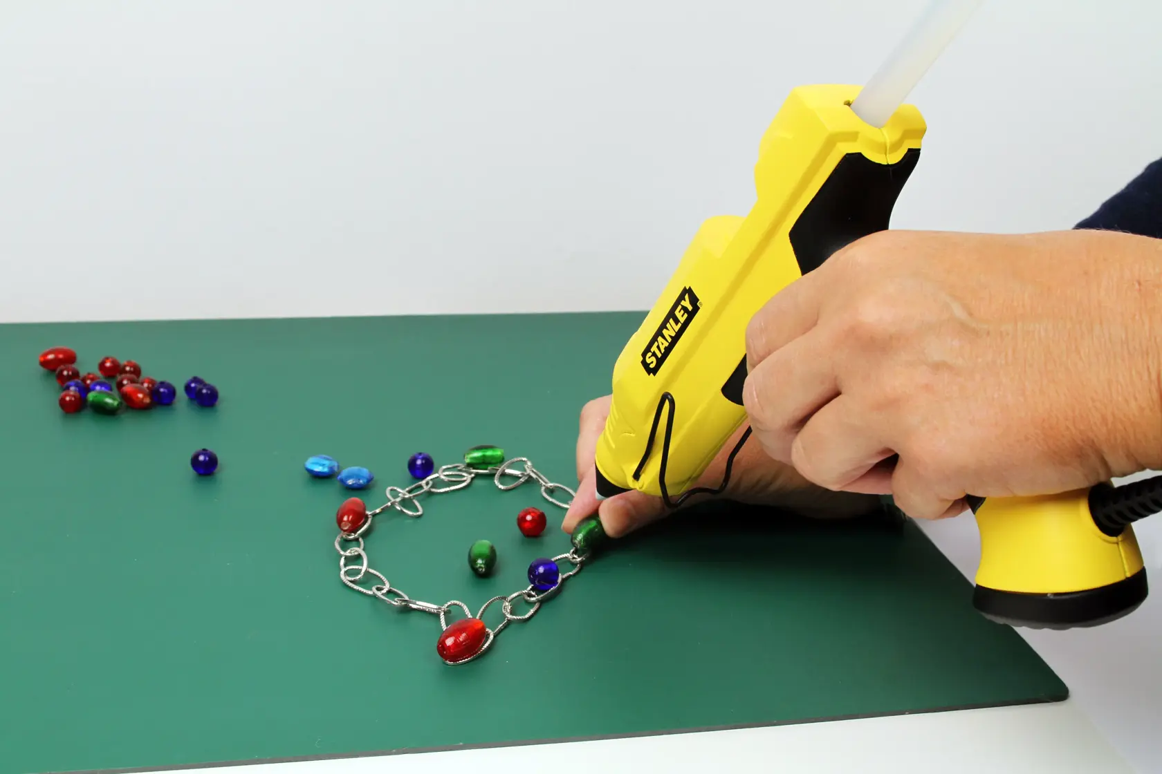 STANLEY STHT6-70417 glue gun in use attaching colorful beads to a metal chain, side angle.