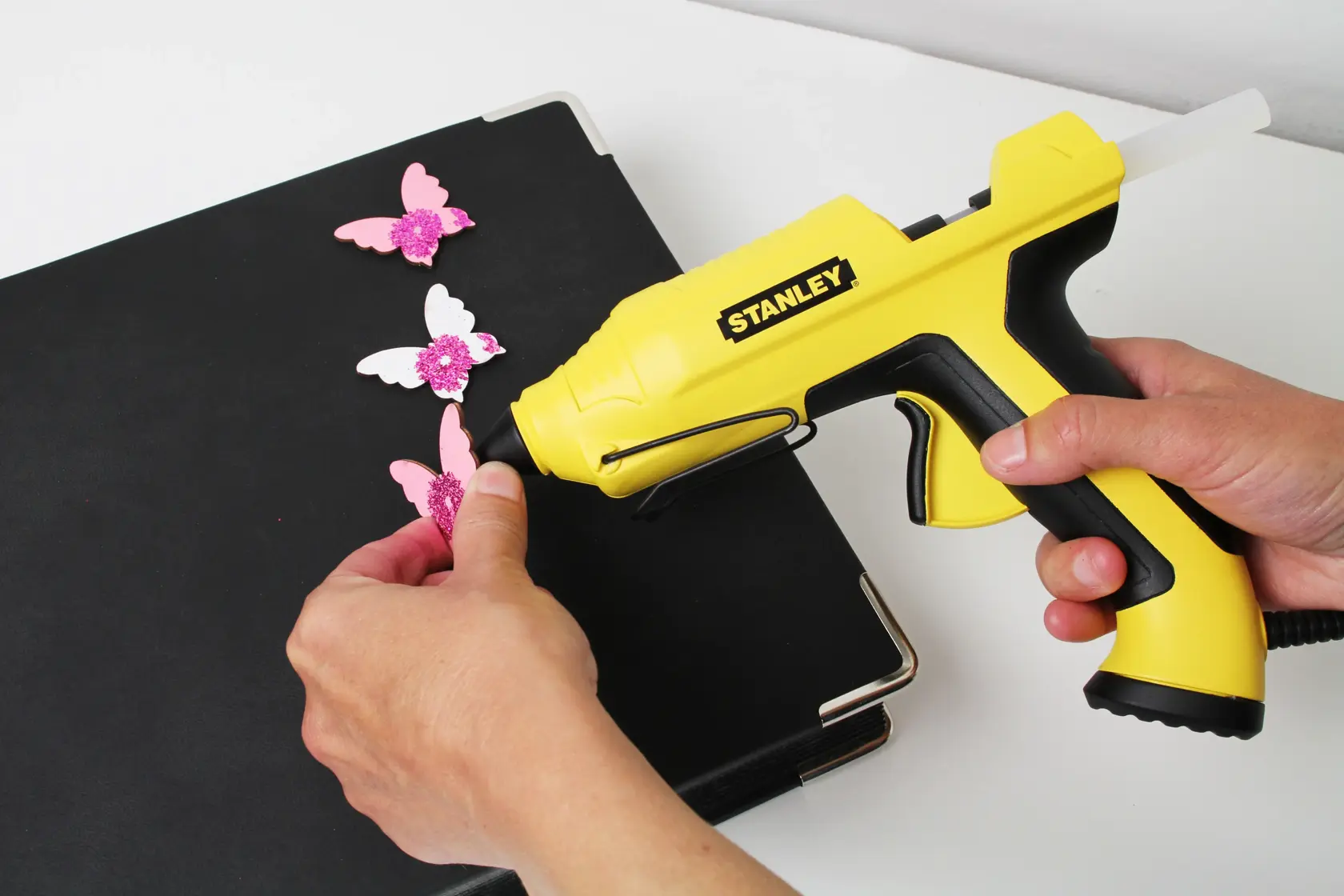 STANLEY STHT6-70417 yellow glue gun used for crafting pink butterfly decorations on a black folder.