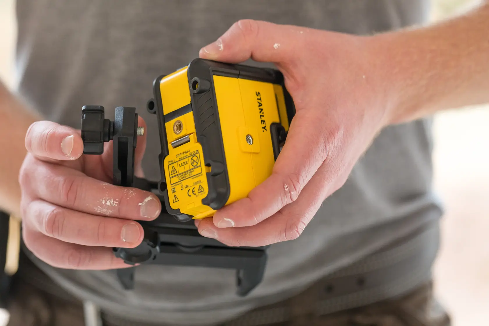 Photo of STANLEY STHT77504-1 yellow and black laser level held in hands, construction context.