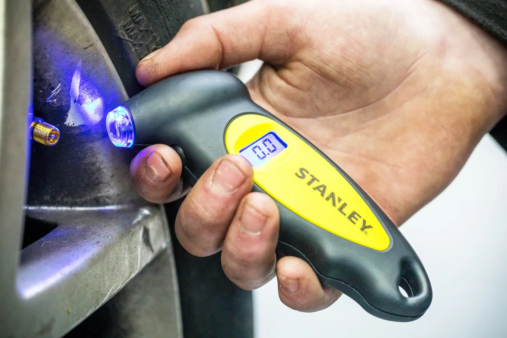 Stanley STHT80874-0 digital tire pressure gauge with blue LED, handheld near tire valve.