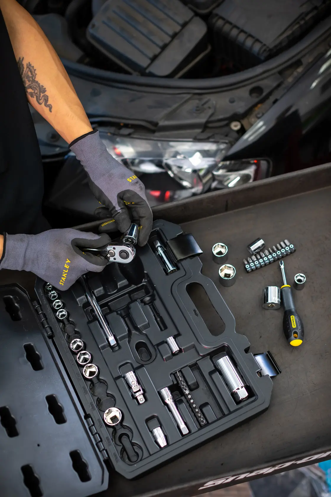 STANLEY STMT82829-1 socket set with ratchet and screwdriver, displayed open by mechanic near car engine.