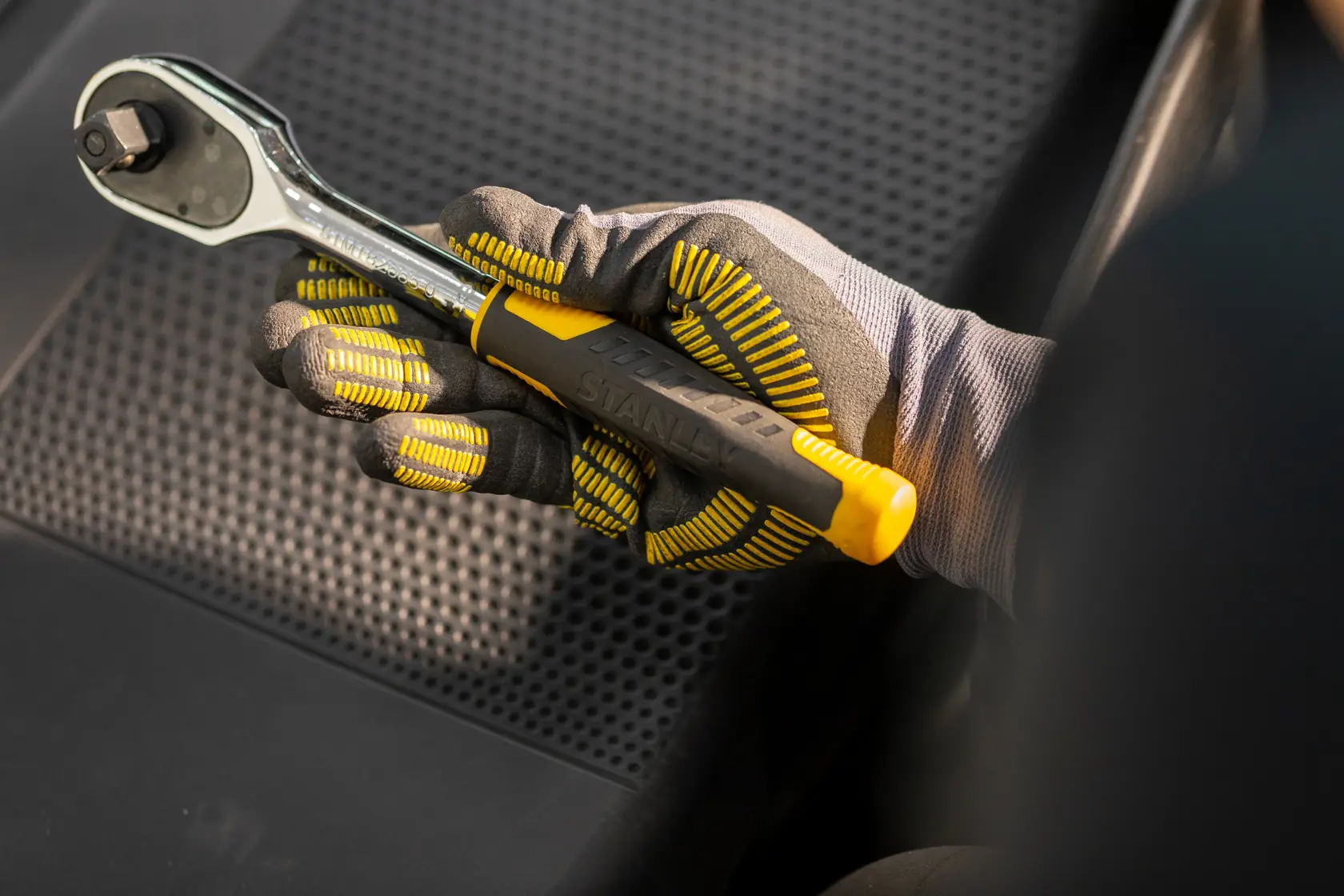 STANLEY STMT82831-1 ratchet wrench with yellow and black handle held by gloved hand, angled view.