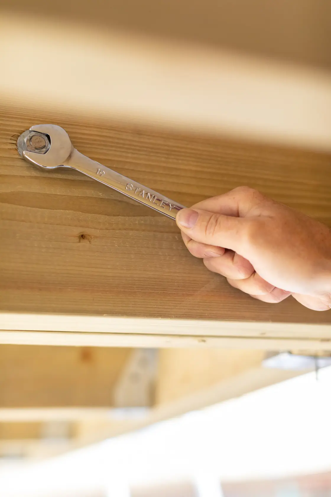 Photo of STANLEY STMT95793-0 combination wrench tightening a bolt on wooden beam.