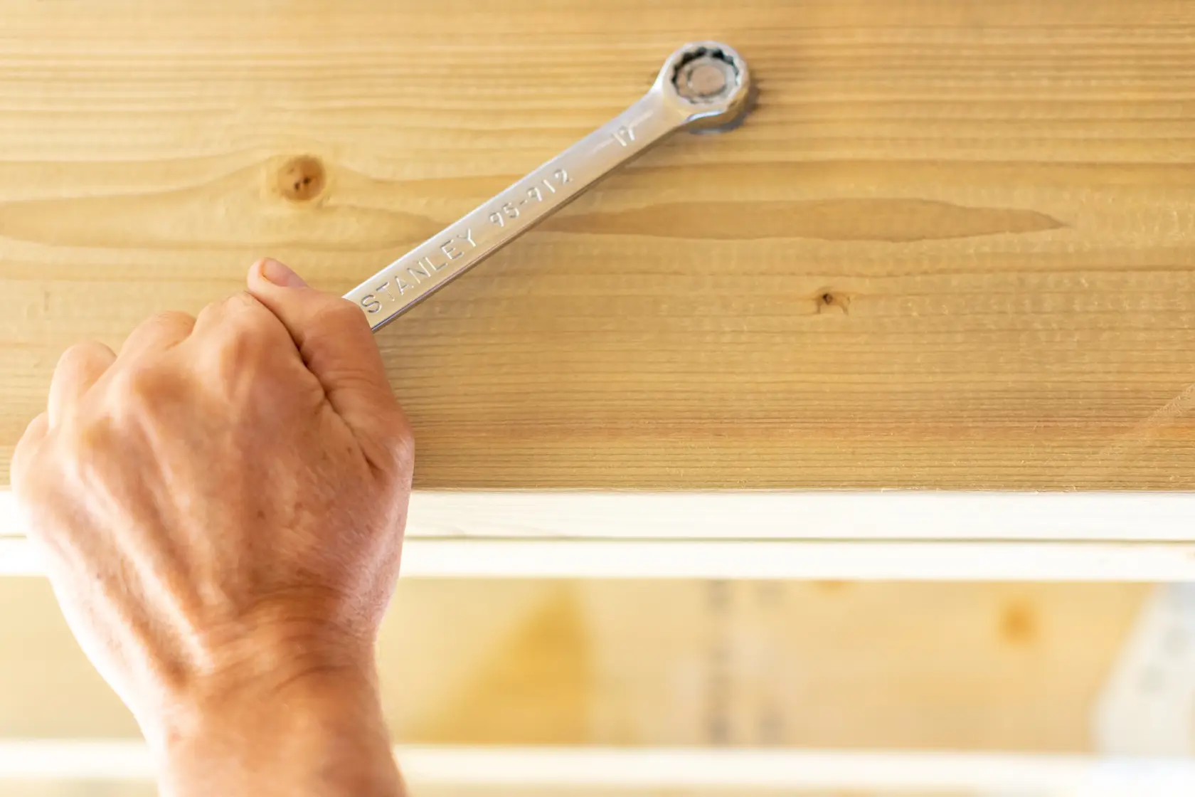 Photo of STANLEY STMT95912-0 ratcheting wrench in use on wood surface, close-up, hand holding tool.