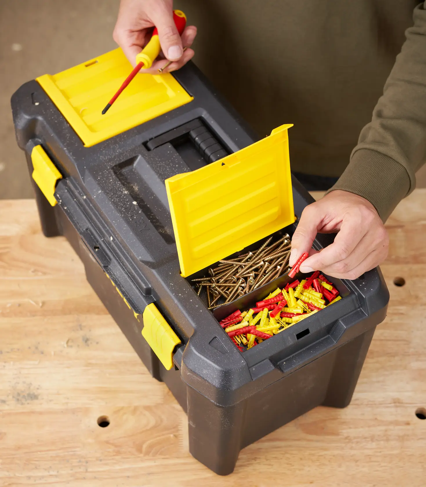 STANLEY STST1-75520 black and yellow toolbox on table, open top compartments with screws and wall plugs, top view.
