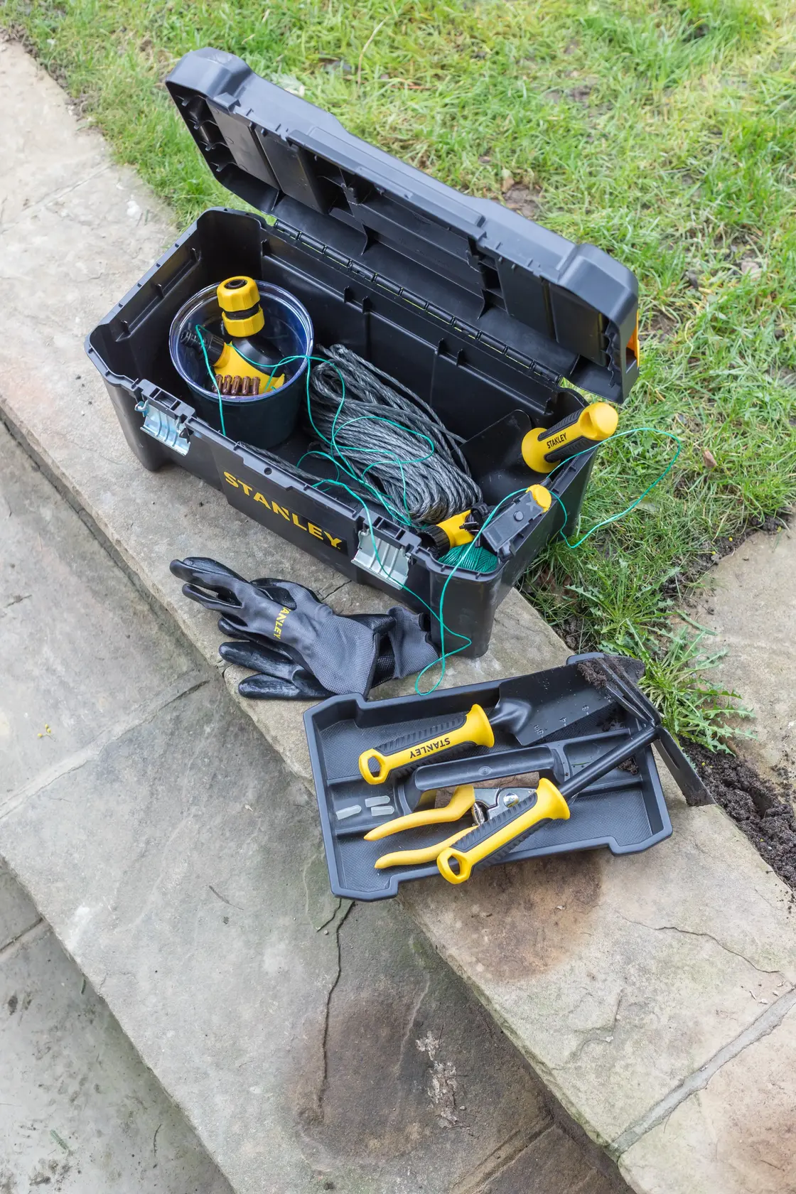Photo of STANLEY STST1-75521 black toolbox with yellow-handled garden tools and gloves, shown outdoors.