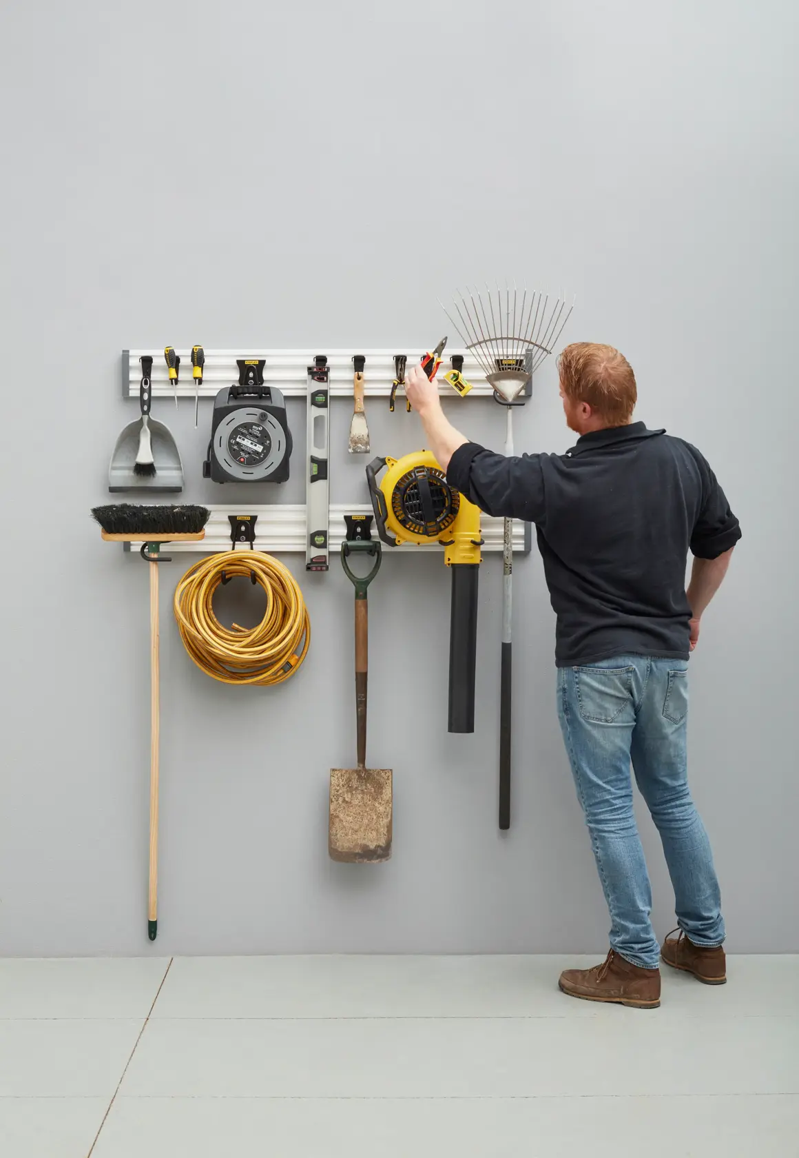 Photo of STANLEY STST22000-1 wall-mounted tool organizer with garden tools and a person arranging items.