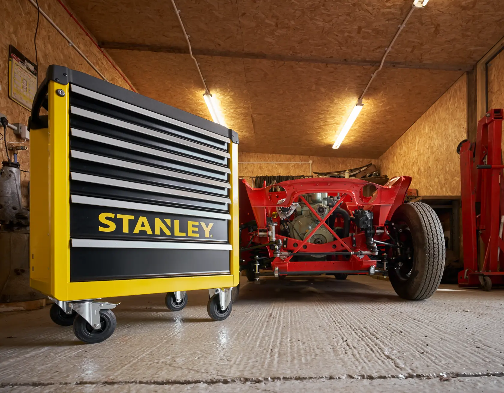 STANLEY STST74306-1 yellow and black rolling tool chest in garage, low angle, near red car frame.