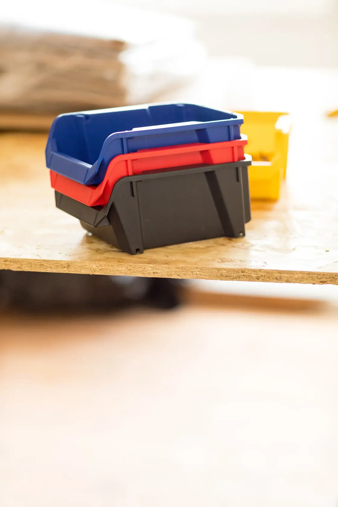 STANLEY STST82737-1 stackable plastic storage bins in black, red, blue, side angle on wooden surface.
