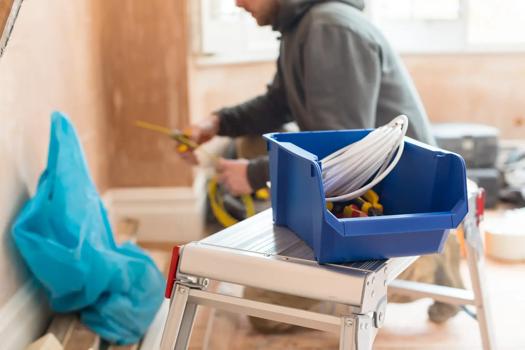 STANLEY STST82743-1 blue storage bin with cables and tools on a step ladder in a workspace.