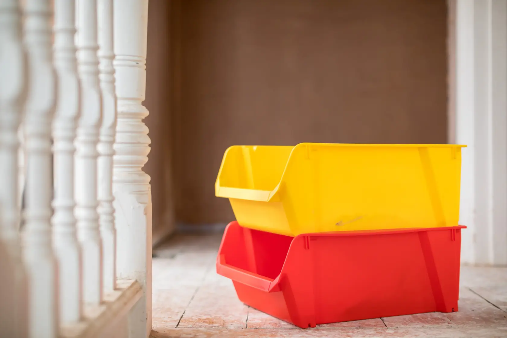 STANLEY STST82745-1 stackable storage bins in yellow and red on a wooden floor, side angle photo.