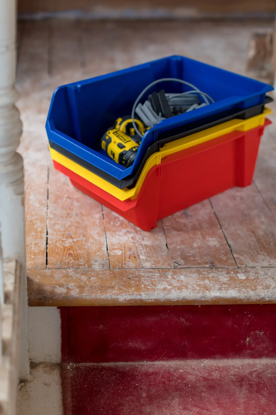 STANLEY STST82745-1 stackable storage bins in red, yellow, and blue with tools on wooden floor.