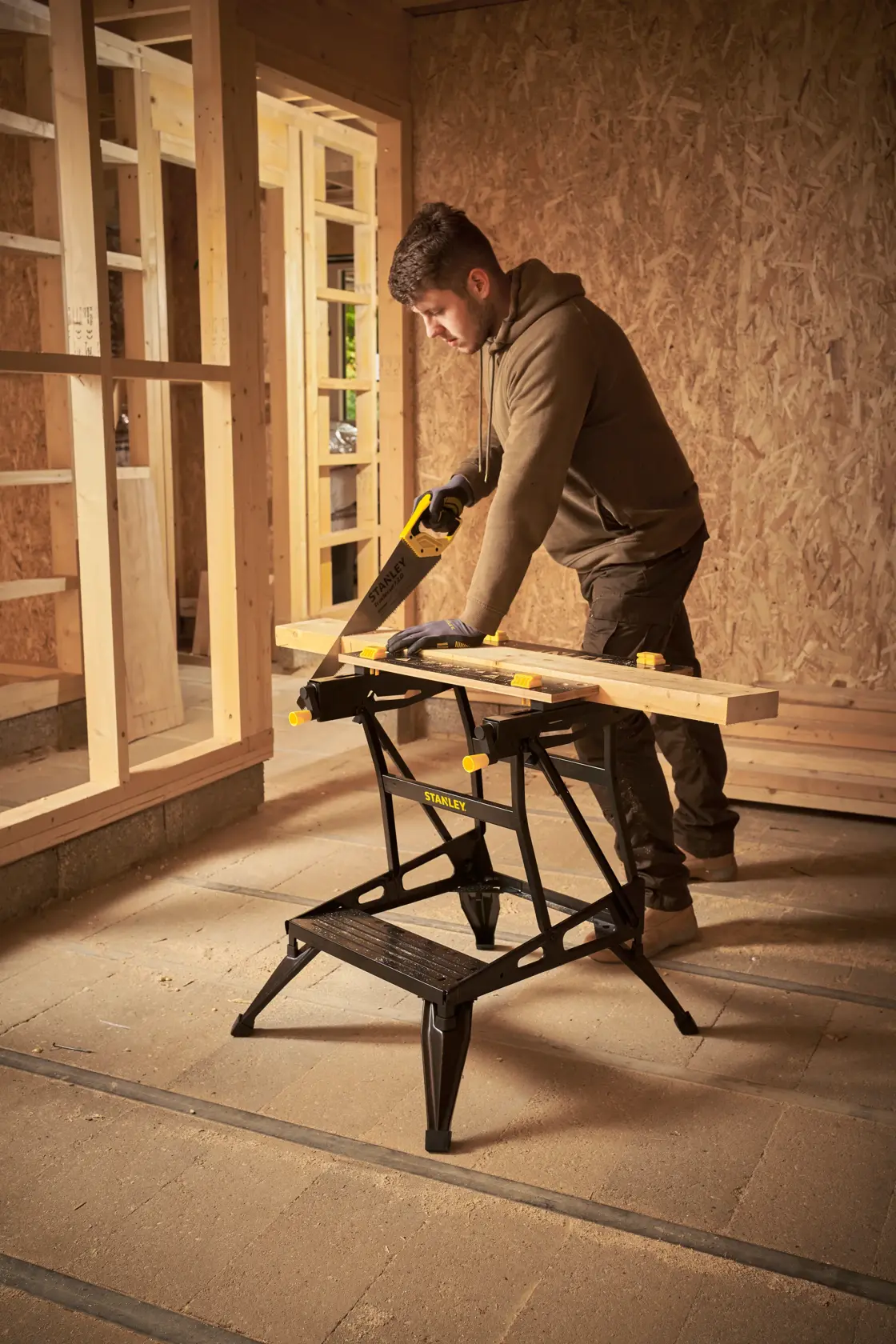 STANLEY STST83400-1 workbench in use, supporting wood for sawing in a construction setting.